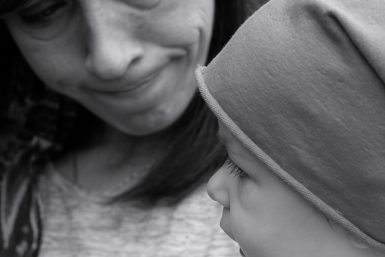 Black and white image of a woman pursing her lips as she holds a baby wearing a hat.